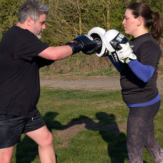 A man and woman practice boxing in a sunny park
