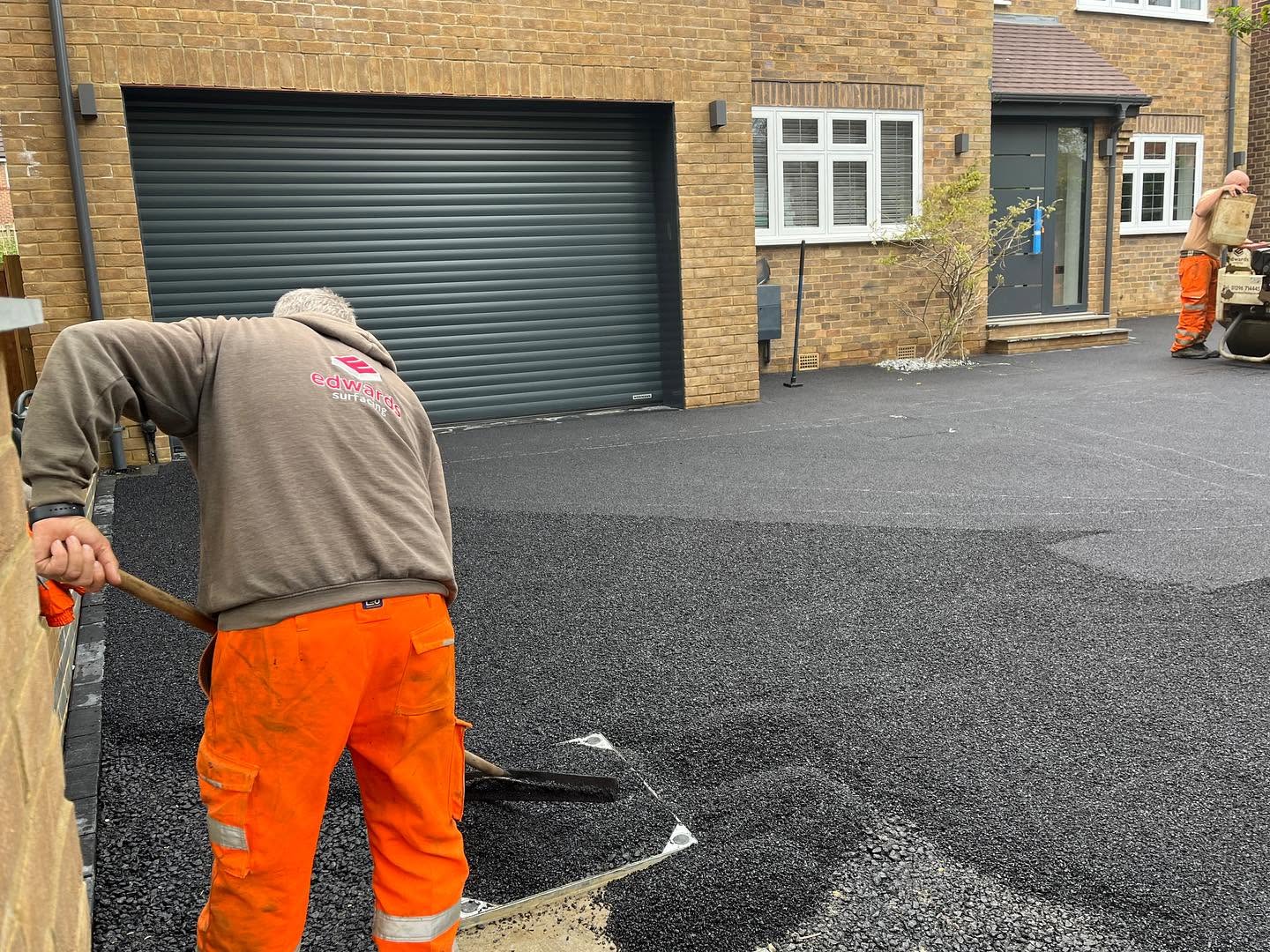 A man in an orange shirt and work boots is repairing a driveway with tools and materials