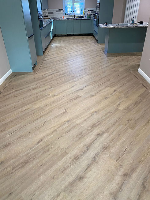 Light oak effect vinyl plank flooring fitted diagonally in a hallway beside blue cupboards