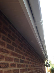 A close-up of a house exterior shows a brick wall with a white soffit and gutter running parallel