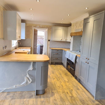 Modern fitted kitchen with grey units, light wooden worktops, integrated appliances, and ceiling spotlights