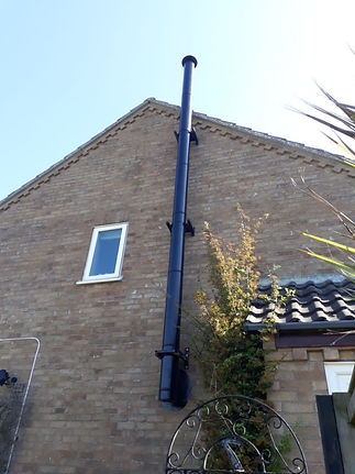 A black chimney pipe is attached vertically to the brick wall of a house