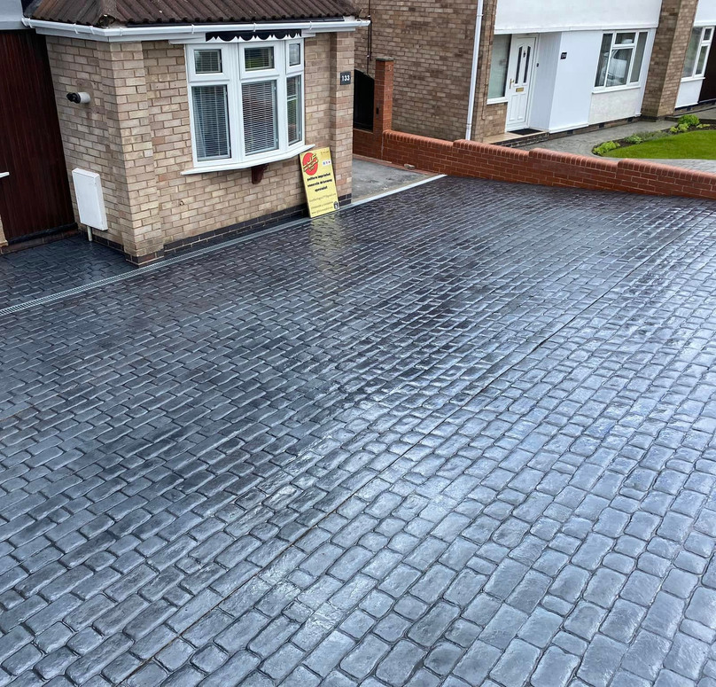 A wet driveway paved with dark gray cobblestones in front of a brick house