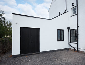 Modern flat-roofed white extension attached to a white building, featuring dark black doors, matching window frames, and black drainpipes