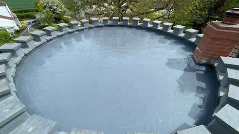 Smooth light grey circular flat roof coating bordered by stone blocks