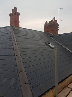 A dark gray slate roof with two red brick chimneys under a cloudy sky