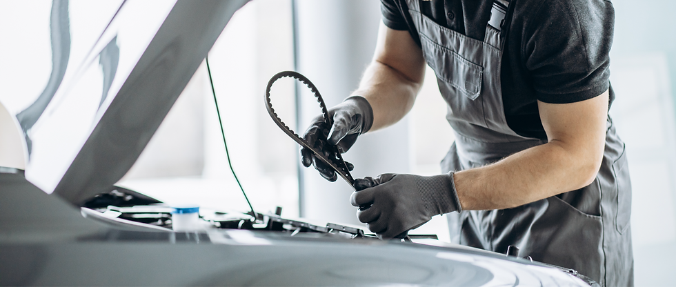Mechanic in grey overalls inspecting a toothed rubber timing belt next to an open car bonnet