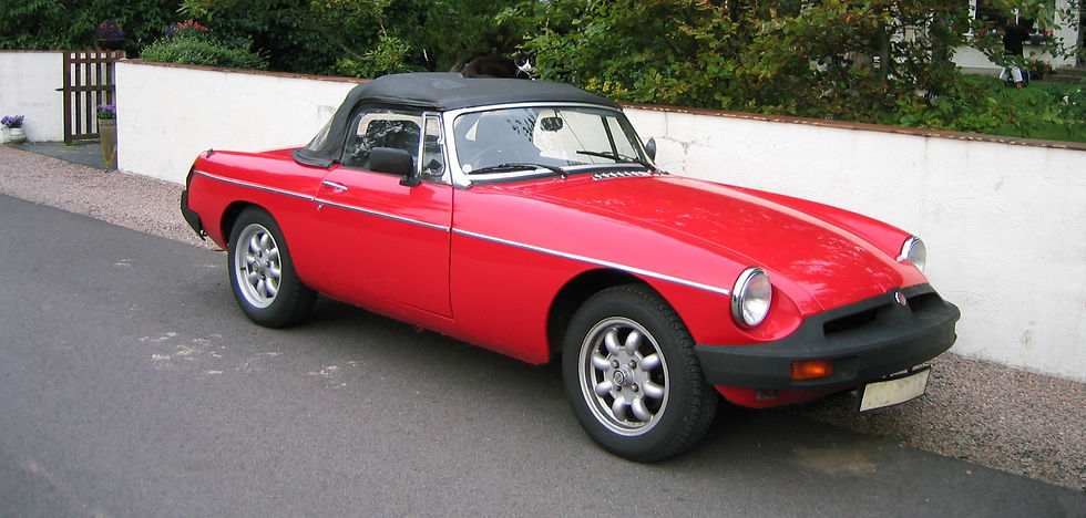 Red vintage convertible car with a black soft top parked beside a white wall