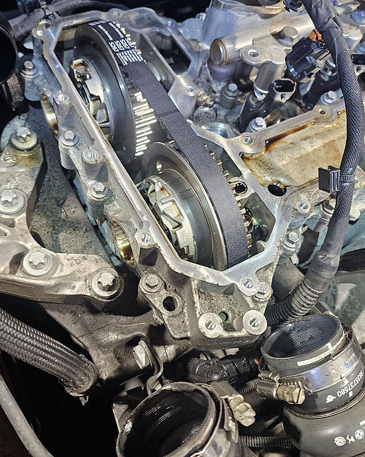 Close-up view of an exposed car engine cylinder head showing a new black timing wet belt fitted around the camshaft gears