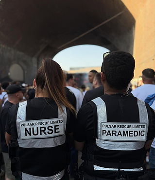 Two individuals in uniforms marked "Nurse" and "Paramedic" stand in a crowd under a large archway, suggesting a vibrant public event or gathering