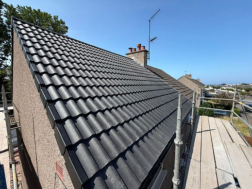 Newly tiled roof with dark grey pantiles, dry verge system, chimney stack, and scaffolding erected alongside