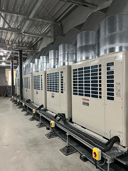 Row of large industrial air conditioning units with silver ductwork on top in a spacious, metallic room, conveying efficiency and modernity
