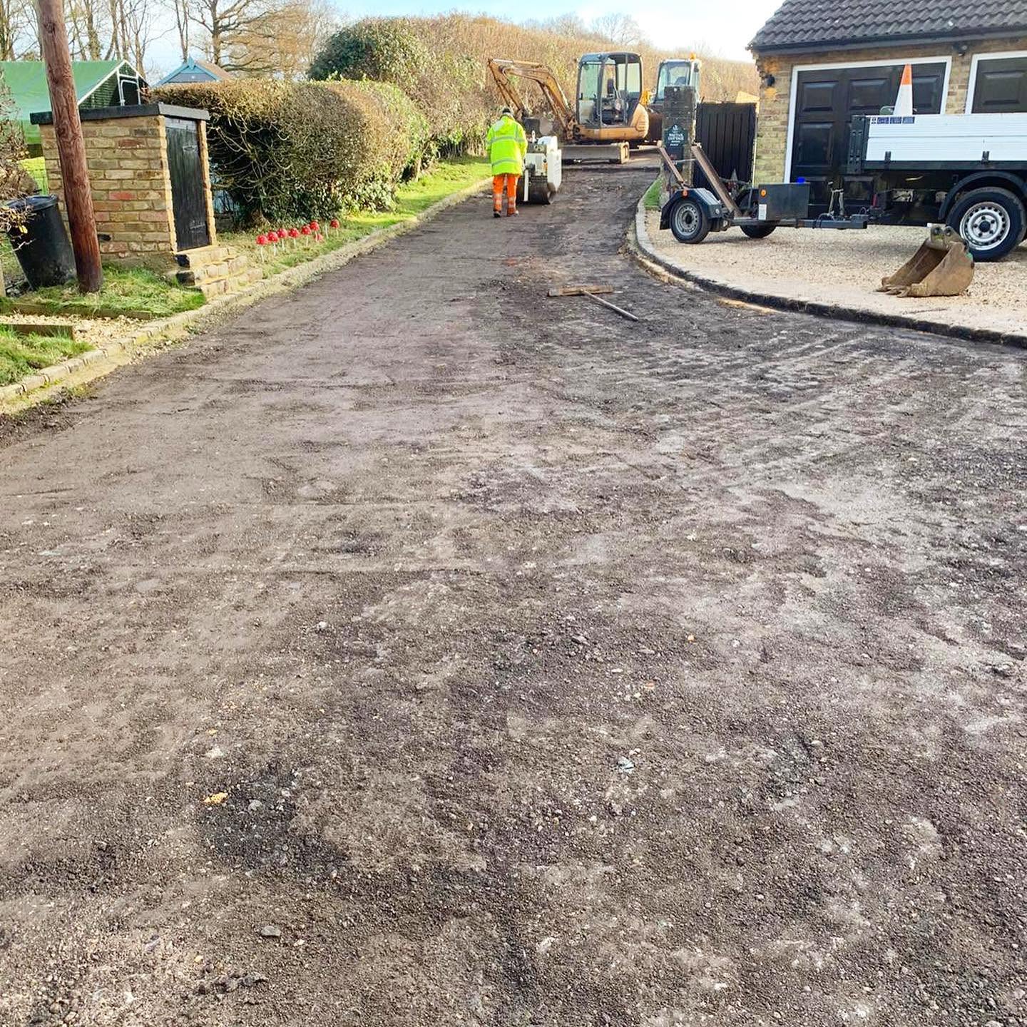 A man is using tools to work on a driveway while a truck is parked nearby