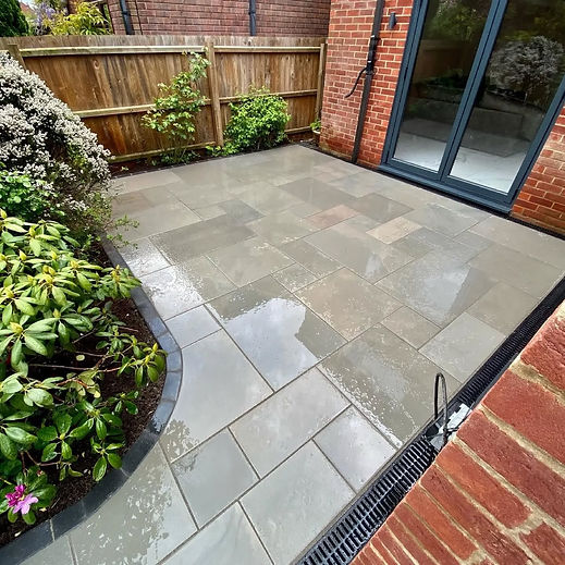 Wet smooth stone patio with curved garden border alongside red brick house and glass doors