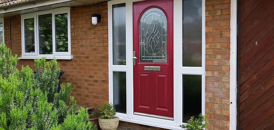 Red front door with decorative glass on a brick house, flanked by tall windows