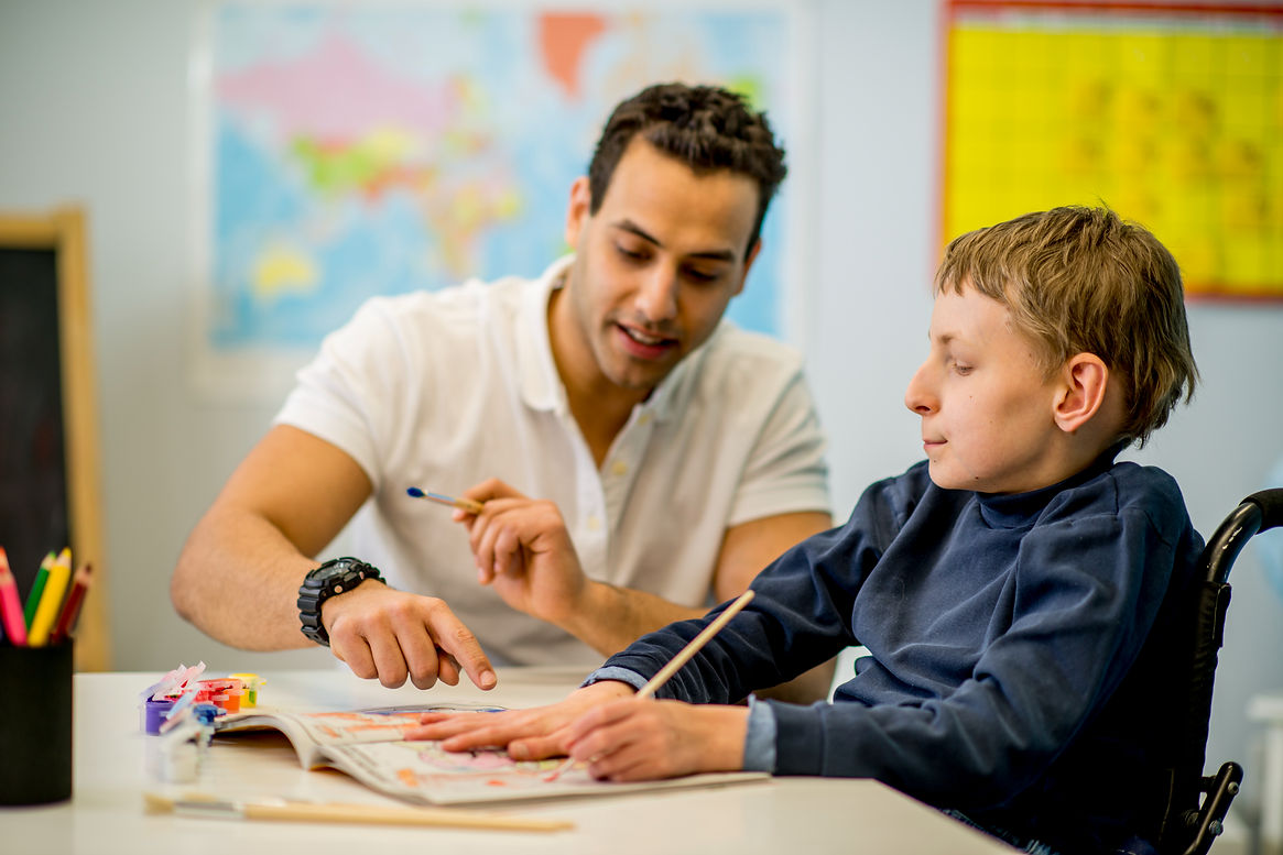Male volunteer supporting a child with chromosome 8P inversion duplication syndrome in a classroom environment