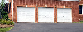 White garage doors set in a red brick wall, with a black paved driveway in front