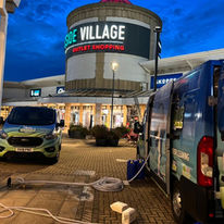 Two vans parked at night outside a shopping center with "Outlet Shopping" signage