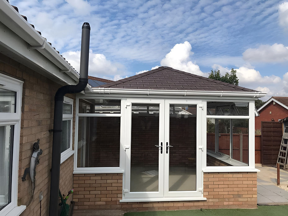A conservatory with a brown tiled roof and white-framed glass doors is attached to a brick house