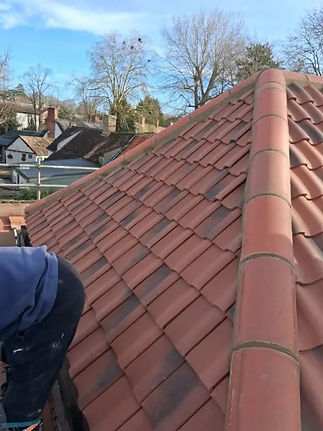 A man is installing red tiles on a roof, focused on his work while standing on a ladder