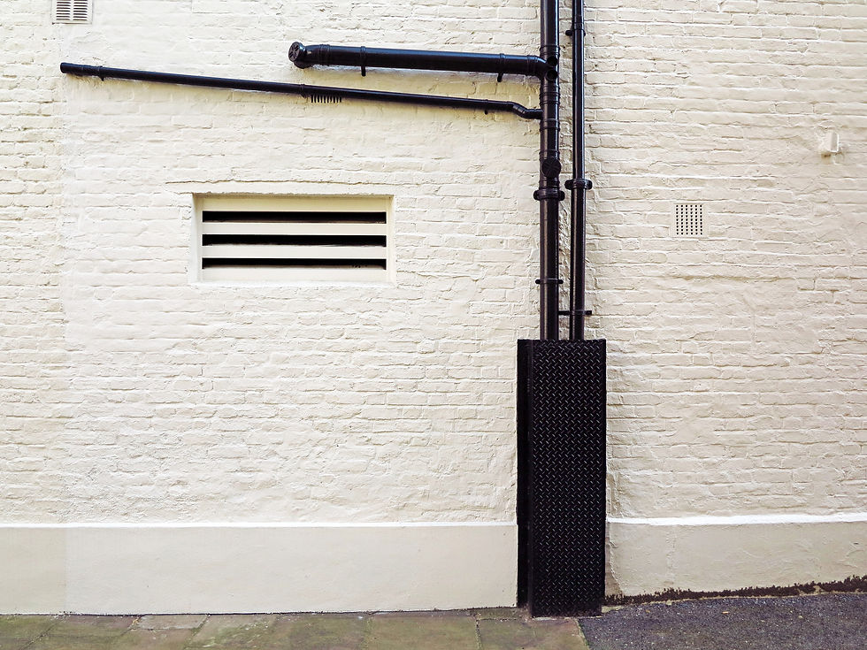 Black drainpipe with metal guard on a white painted brick wall