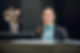 A smiling hotel receptionist with a blue scarf stands at a dark wood desk