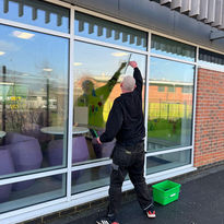 A person cleans large glass windows with a squeegee outside a building
