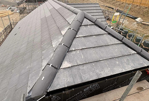 High-angle view of a slate roof construction with dry ridge and hip systems installed on a newly built structure