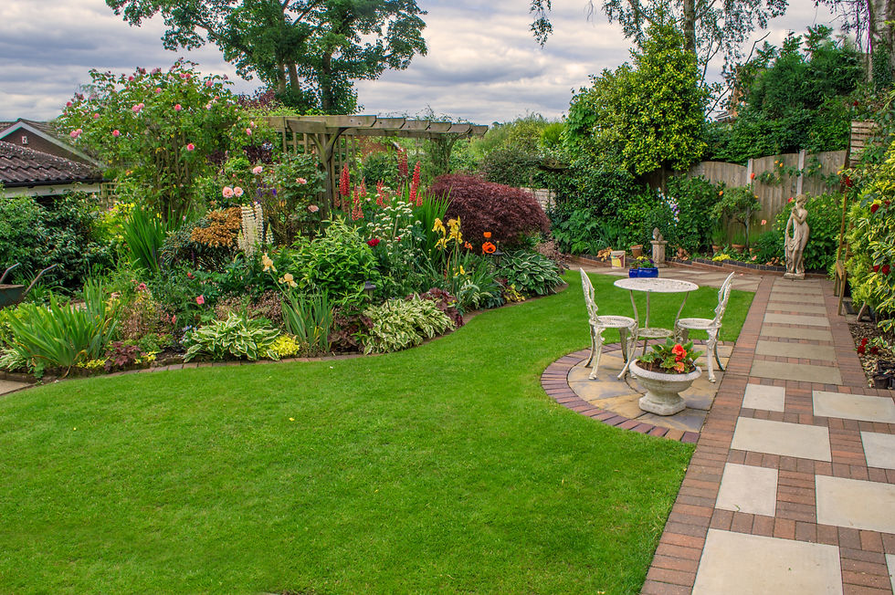 Landscaped backyard featuring a paved pathway, a small patio with outdoor seating, a green lawn, and flower beds with a pergola