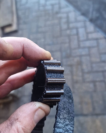 Close-up of a mechanic holding a heavily cracked and damaged black rubber wet belt showing severe wear and tear