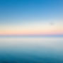 Calm ocean at sunset with a gradient sky of soft pink and blue hues