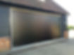 leek black roller garage door on a brick-wall building, partially opens, reflecting sunlight