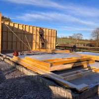 Construction site under a clear blue sky, with workers assembling wooden panels on a concrete foundation