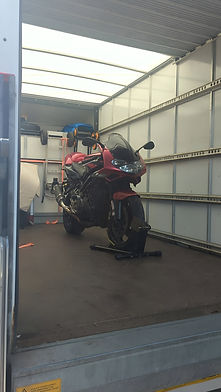 A red motorbike secured on a wheel stand inside the back of an empty removal lorry