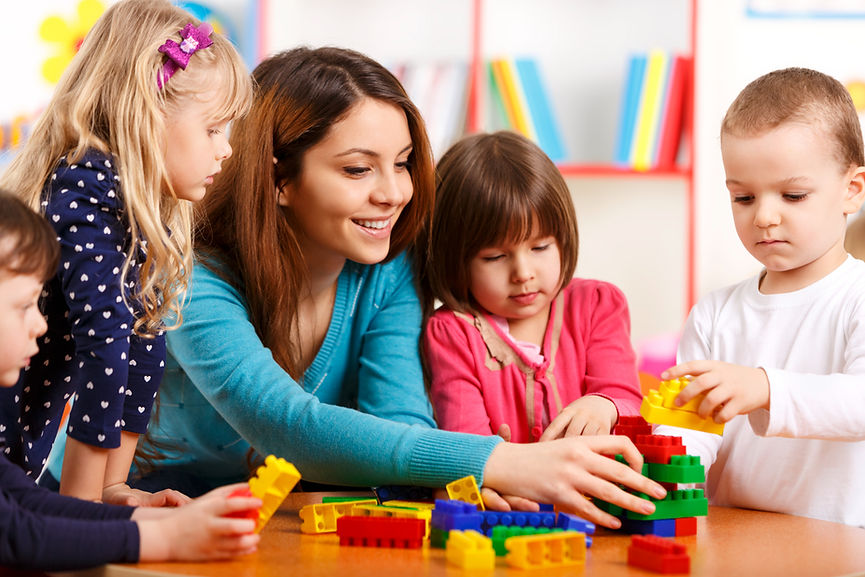 A woman and four children are playing with colorful building blocks at a table