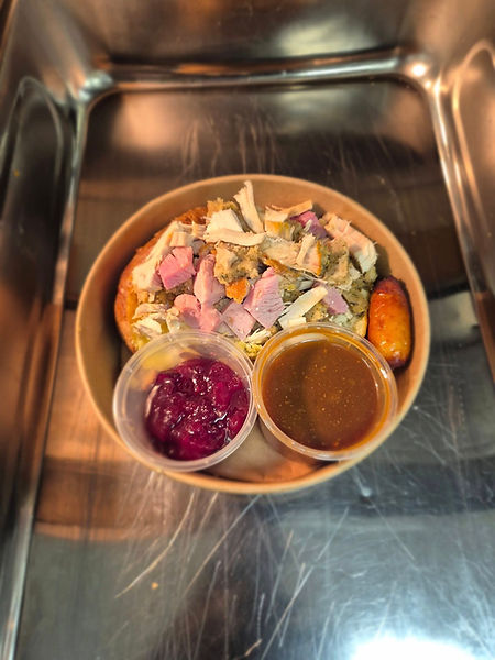 A round bowl of sliced turkey, stuffing, and a sausage is placed on a metal surface