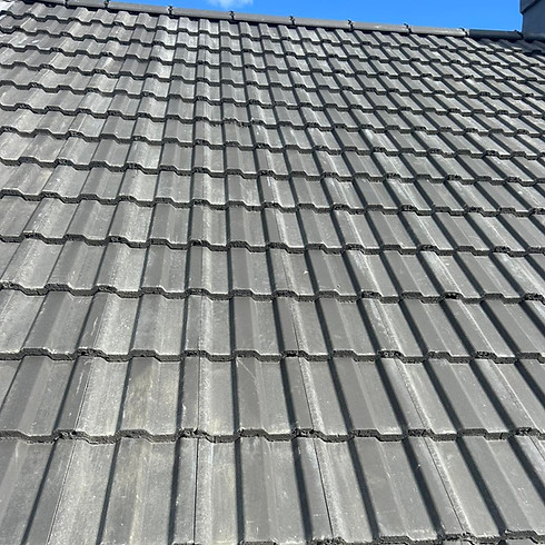 Gray, textured roof tiles under bright sunlight, casting shadows that create a striped pattern