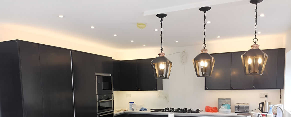 Modern kitchen with sleek black cabinets and appliances, accented by three lantern-style pendant lights
