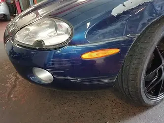 Close-up of a blue car's front bumper with noticeable scratches and scuffs