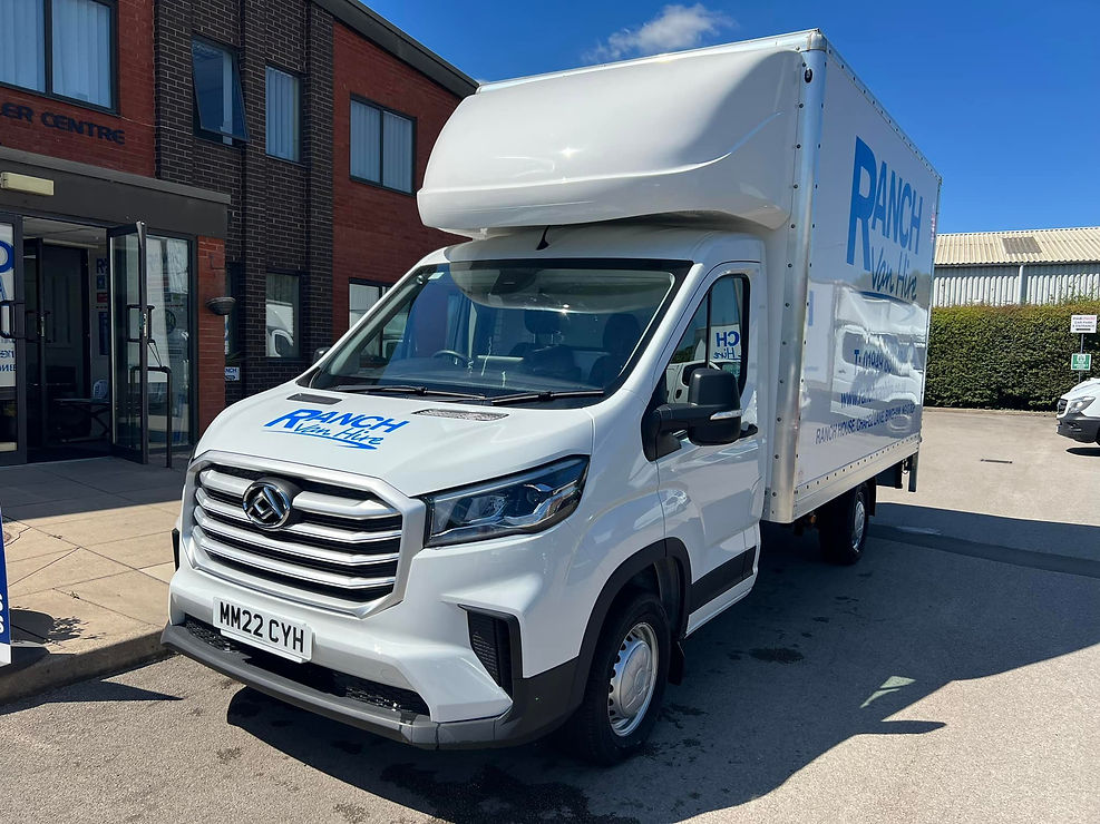 White rental van with "Ranch Van Hire" logo parked outside a brick building on a sunny day