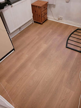 Warm wood-effect vinyl flooring fitted neatly next to a dark wall trim and metal stand