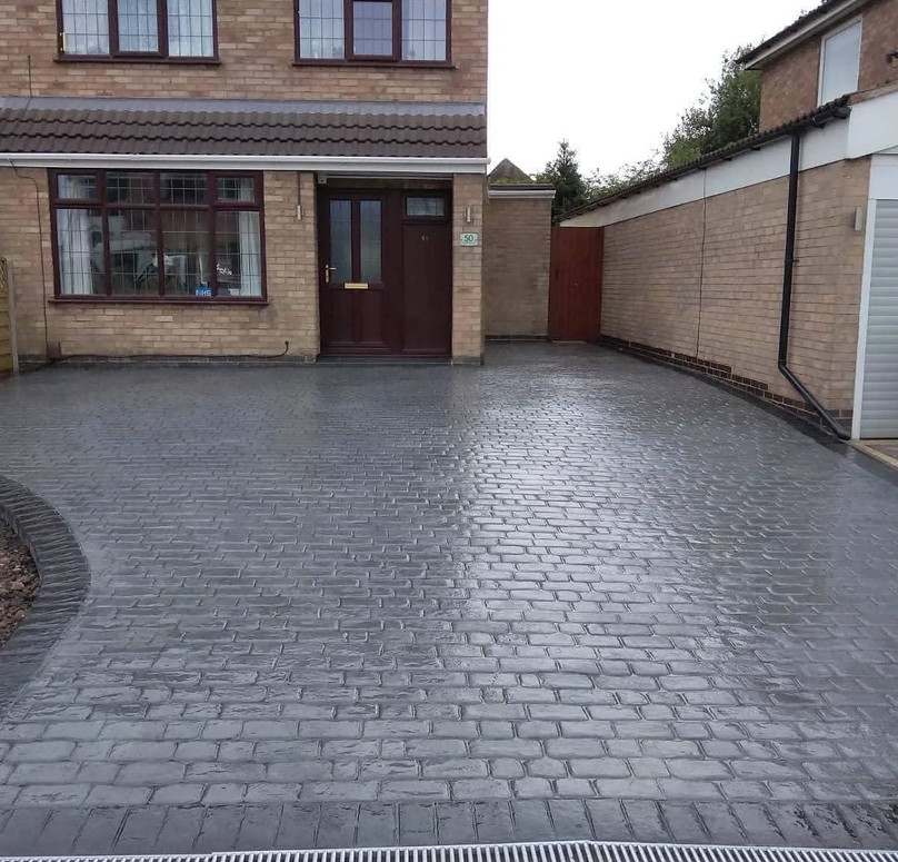 Driveway of a brick house, paved with gray cobblestones, leading to a brown door