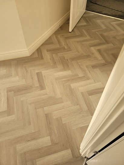 Light oak vinyl flooring laid out in a classic herringbone parquet pattern