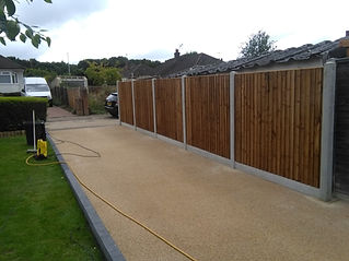 A neat gravel driveway bordered by a lush green lawn and wooden fence panels with concrete posts