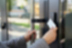 A person in a gray coat uses a keycard to unlock a modern glass door