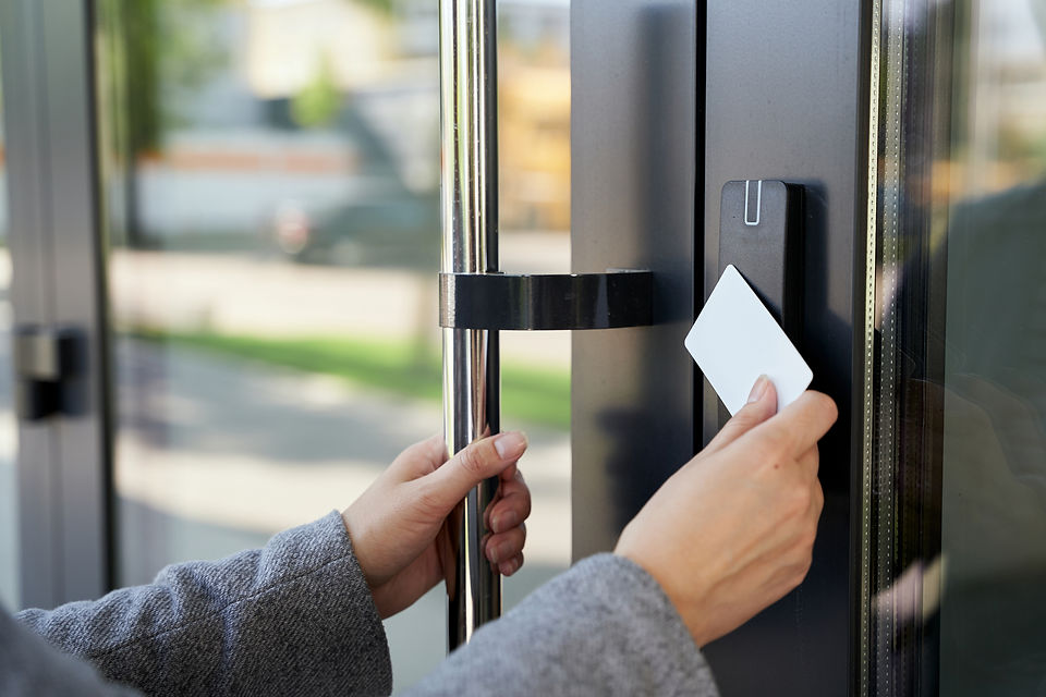A person in a gray coat uses a keycard to unlock a modern glass door