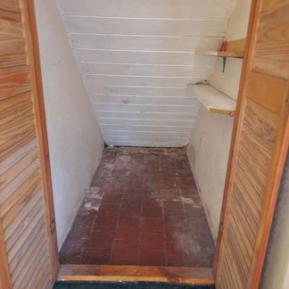 Narrow closet with sloped ceiling, wooden doors, tiled floor, and small shelves on the right wall