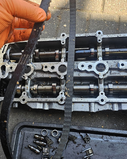 Gloved hand holding a worn black wet belt over exposed engine camshafts during a repair