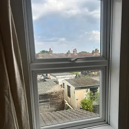 View of rooftops and chimneys through a window from a room with beige curtains
