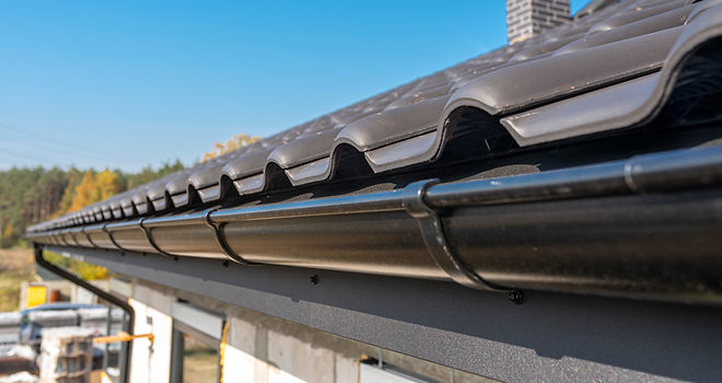 Close-up of clean black plastic uPVC roof gutters attached to dark grey roof tiles